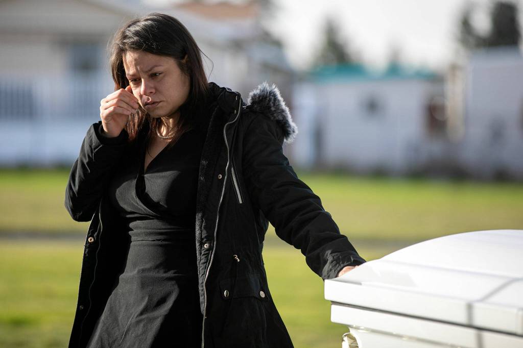 Betsy Alvarado brushes her hand along the casket of one of her daughters during their funeral Friday, Jan. 28, 2022, at Cypress Lawn Memorial Park in Everett. (Ryan Berry / The Herald)
