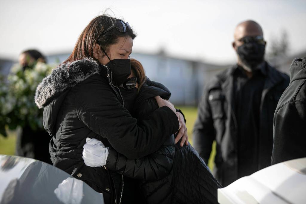 Betsy Alvarado and Irma Amundson, mother and grandmother to Adriana and Mariel Gil, respectively, hug over the girls grave during a funeral Friday, Jan. 28, 2022, at Cypress Lawn Memorial Park in Everett. (Ryan Berry / The Herald)