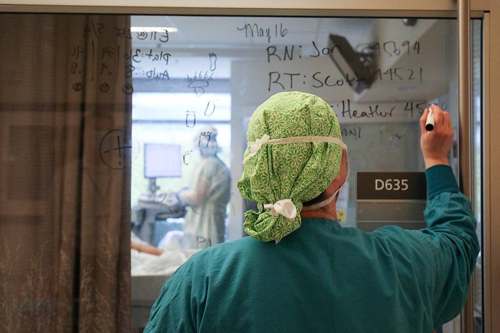 A Providence Regional Medical Center Everett employee writes a patients vitals outside of their room on May, 19, 2020. (Andy Bronson/ Herald file)