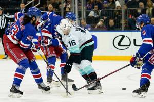 Seattle Kraken left wing Jared McCann (16) is triple-teamed by New York Rangers center Mika Zibanejad (93), left wing Alexis Lafrenière (13), and defenseman Jacob Trouba (8) during the first period of an NHL hockey game, Sunday, Jan. 30, 2022, in New York. (AP Photo/John Minchillo)