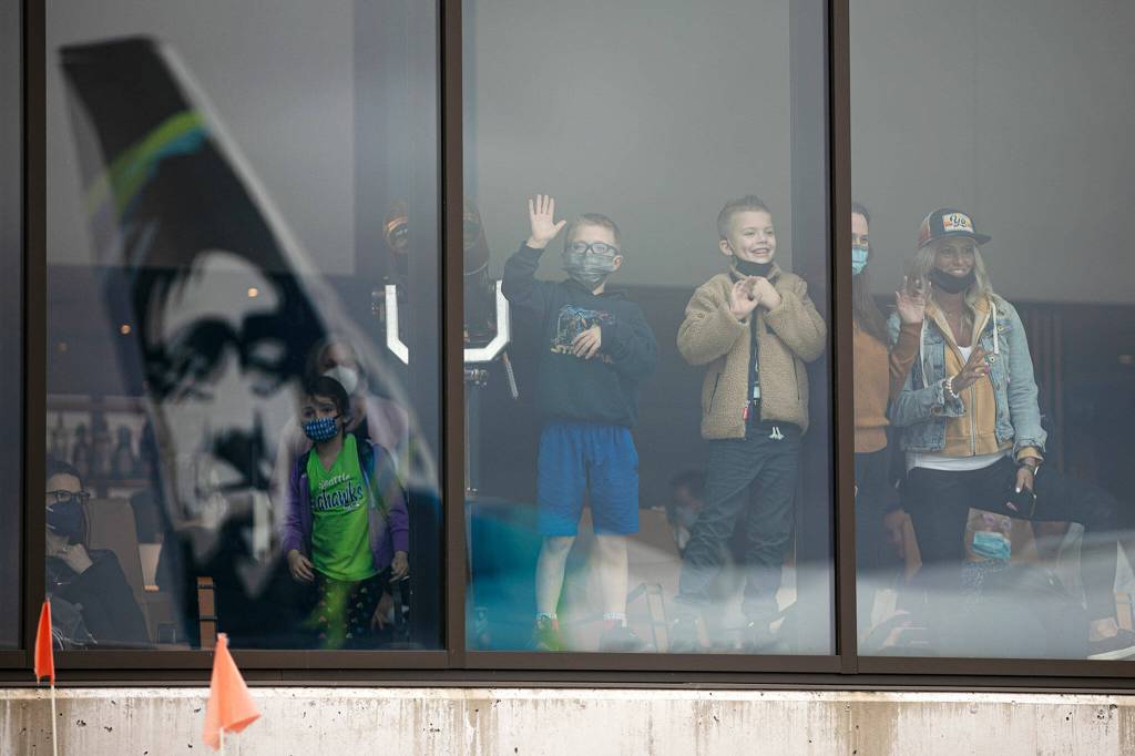 People inside the airport wave to passengers aboard the first Alaska Airlines Boeing 737 arrival Thursday at Paine Field Airport in Everett. (Ryan Berry / The Herald)