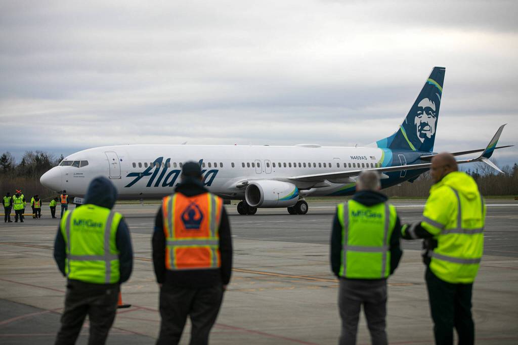 Airport workers watch as an Alaska Airlines Boeing 737 embarks on the first 737 flight out of Paine Field on Thursday in Everett. (Ryan Berry / The Herald)