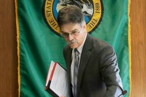 Steve Lerch, executive director of the Washington state Economic and Revenue Forecast Council, walks in front of the Washington state flag, Wednesday, Feb. 19, 2020, following a meeting of the council at the Capitol in Olympia, Wash. Lawmakers were told that the state's latest revenue forecast shows they have significantly more money to work with as they prepare to unveil their supplemental state budget proposals. (AP Photo/Ted S. Warren)