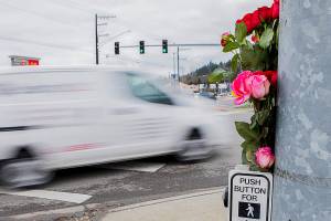 A car drives by flowers placed at a memorial for two pedestrians killed at the corner of 204th Street NE and Highway 9 on Friday, Jan. 21, 2022 in Arlington, Washington. (Olivia Vanni / The Herald)