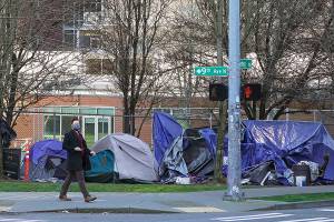 FILE - In this March 3, 2021, file photo, with apartment buildings in the background, pedestrians walk past tents used by people lacking housing at Denny Park near the Space Needle in Seattle, after the park was cleared by city workers of several dozen tents. Backers of a measure that would change Seattle's approach to homelessness are appealing a judge's decision that blocked it from the November ballot. The proposal would direct the city to provide 2,000 units of housing within a year and to keep public land clear of encampments. (AP Photo/Ted S. Warren, File)