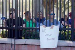 Baseball fans watch as Major League Baseball Commissioner Rob Manfred speaks during a news conference after negotiations with the players' association toward a labor deal, Tuesday, March 1, 2022, at Roger Dean Stadium in Jupiter, Fla. Manfred said he is canceling the first two series of the season that was set to begin March 31, dropping the schedule from 162 games to likely 156 games at most. Manfred said the league and union have not made plans for future negotiations. Players won't be paid for missed games. (AP Photo/Wilfredo Lee)