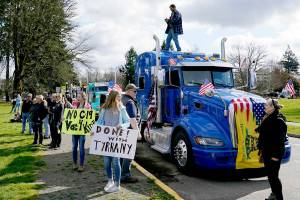 People hold signs as they stand near parked semi-trucks during a protest against COVID-19 vaccine mandates and other issues, Saturday, March 5, 2022, at the Capitol in Olympia, Wash. The trucks were part of a local convoy that traveled to Olympia for the protest. (AP Photo/Ted S. Warren)