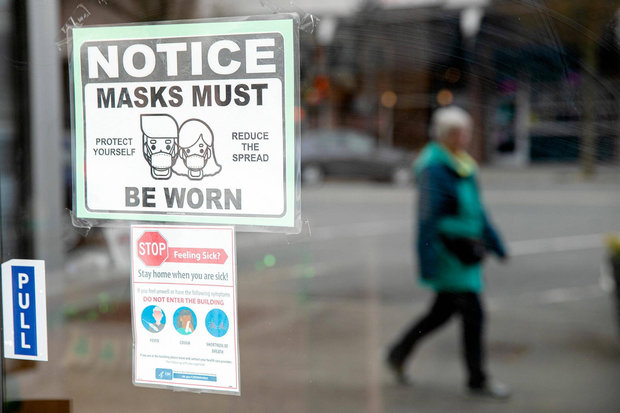 A woman walks past a downtown business with a sign requiring customers to wear masks Thursday in Everett. (Ryan Berry / The Herald)