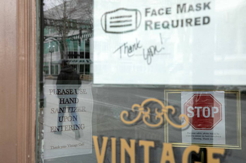 A sign inside Vintage Cafe asks customers to use hand sanitizer, while a message requiring face masks is posted to the door Thursday in Everett. (Ryan Berry / The Herald)
