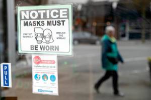 A woman walks past a downtown business with a sign requiring customers to wear masks Thursday, March 10, 2022, in Everett, Washington. (Ryan Berry / The Herald)