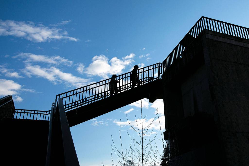 Two pedestrians cross above the train tracks near the Lowell Riverfront Trail during a clear and breezy Friday afternoon in Everett. (Ryan Berry / The Herald)