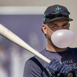 Seattle Mariners' Eugenio Suarez blows a bubble as he waits to bat during spring training baseball practice Wednesday, March 16, 2022, in Peoria, Ariz. (AP Photo/Charlie Riedel)