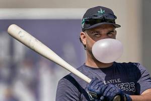 Seattle Mariners' Eugenio Suarez blows a bubble as he waits to bat during spring training baseball practice Wednesday, March 16, 2022, in Peoria, Ariz. (AP Photo/Charlie Riedel)