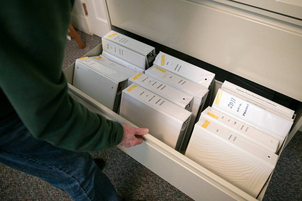 Mukilteo Historical Society volunteer Peter Anderson rifles through binders of images from the towns history. (Ryan Berry / The Herald)