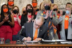 Washington Gov. Jay Inslee signs a bill that bans the manufacture, distribution and sale of firearm magazines that hold more than 10 rounds of ammunition in Washington state, Wednesday, March 23, 2022, at the Capitol in Olympia, Wash., as his wife Trudi, center-right, and other supporters applaud. The measure was one of three in a package of bills tightening the state's gun laws that were signed Wednesday. (AP Photo/Ted S. Warren)