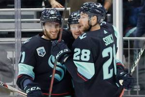 Seattle Kraken center Alex Wennberg, left and defenseman Carson Soucy (28) embrace left wing Jared McCann after he scored against the Dallas Stars during the first period of an NHL hockey game Sunday, April 3, 2022, in Seattle. (AP Photo/John Froschauer)