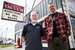 Mike Lane and son Dave Lane, right, in front of their family store Everett Vacuum with their popular sign and saying, “everything we sell sucks” on Thursday, April 7, 2022, in Everett, Washington. (Olivia Vanni / The Herald)