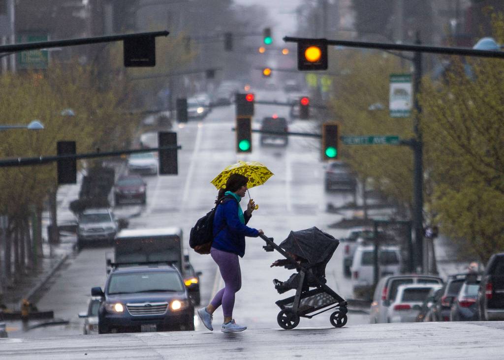 A woman quickly crosses Hoyt Avenue while pushing a stroller as it starts to rain heavily on March 30 in Everett. (Olivia Vanni / The Herald)