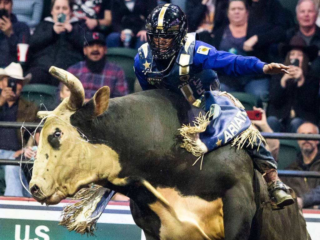 Ezekiel Mitchell leans forward while his bull leaps in the air during the PBR Everett Invitational at Angel of the Winds Arena on Wednesday, April 6, 2022 in Everett, Washington. (Olivia Vanni / The Herald)
