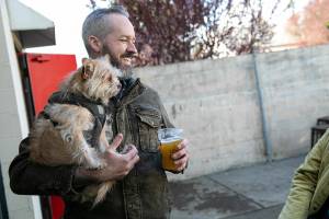 Chris Langford holds onto 5-year-old Fezzik while enjoying a beer during Pints and Pups’ grand opening Saturday, April 9, 2022, in Everett, Washington. (Ryan Berry / The Herald)
