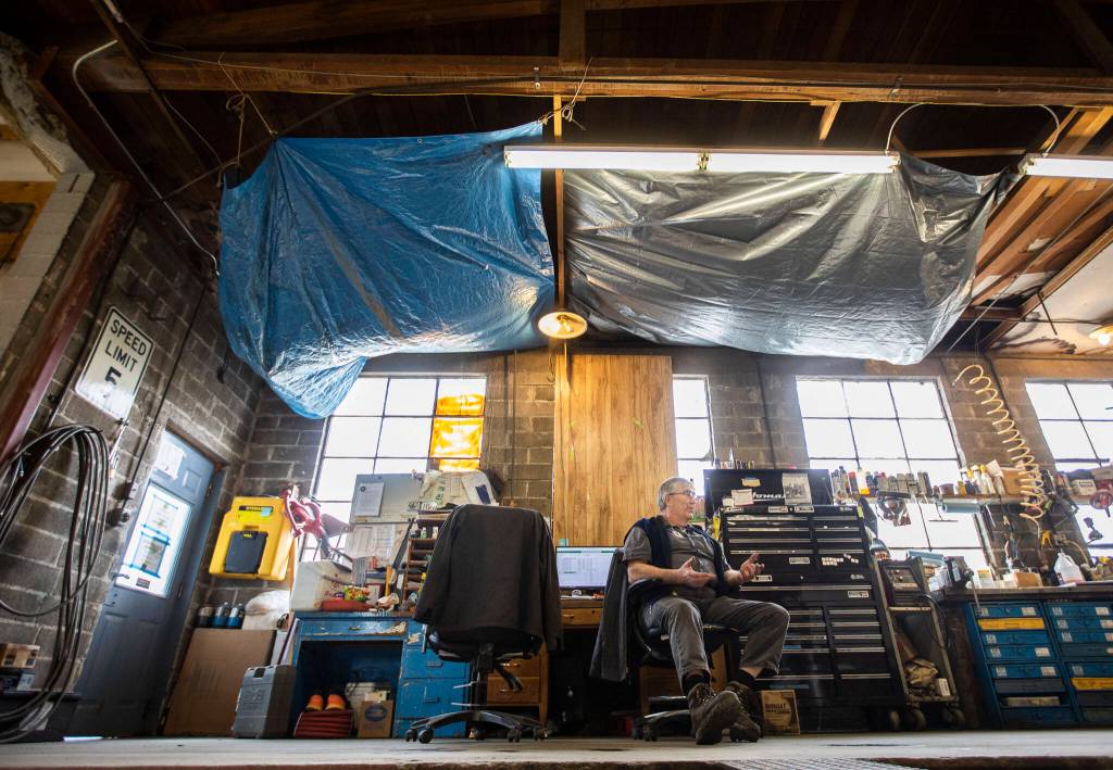 Dan Erdman sits beneath tarps that hang from the bus barn ceiling to help catch water that leaks through the roof. (Olivia Vanni / The Herald)