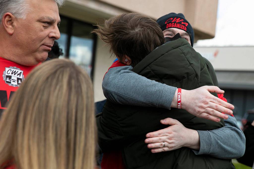Austin Hitch and Jesse Mason hug after an 11-1 vote in favor of unionizing Friday at a Verizon store in Everett. (Ryan Berry / The Herald)
