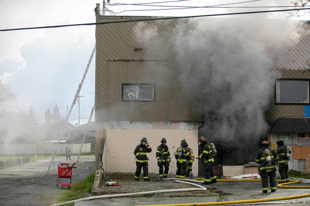Firefighters stand outside a lower level garage at 9629 Evergreen Way as smoke billows out of it Thursday, April 13, 2022, in Everett, Washington. (Ryan Berry / The Herald)