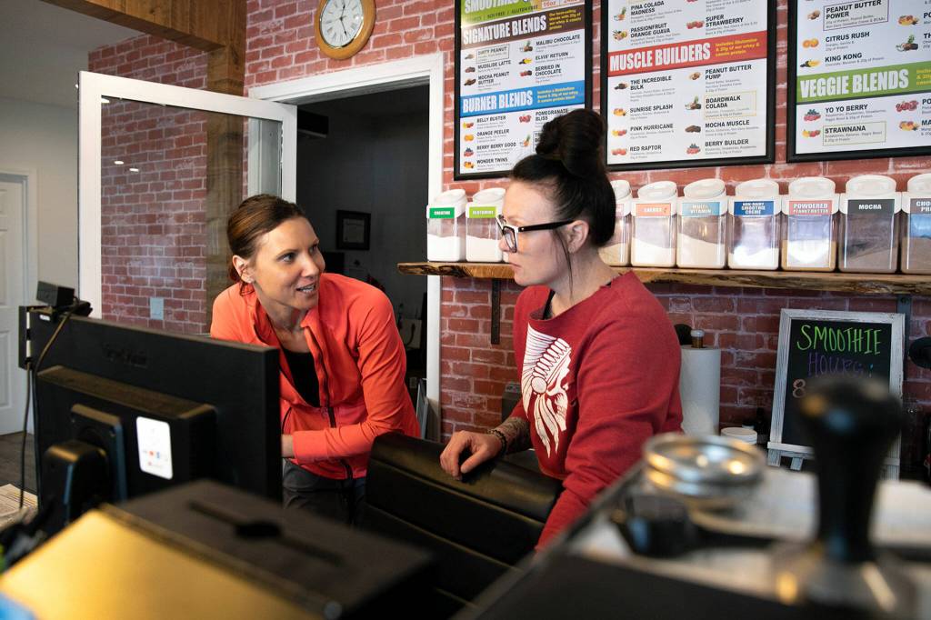 Co-owner of J.B. Fitness Candice Blair (left) talks with employee Kathryn Agnew at the front desk of the recently relocated business Thursday in Sultan. (Ryan Berry / The Herald)
