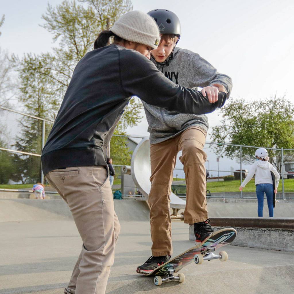 Brandon Garcia-Zuniga (left) guides Logan Little during a skateboard workshop April 28 at Wiggum Hollows Park in Everett. (Kevin Clark / The Herald)