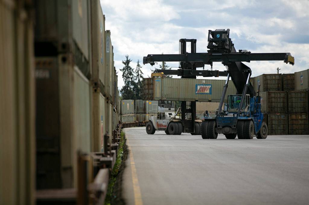 Two machines move bins filled with county trash around a shipping yard Friday, April 29, 2022, along the Snohomish River in Everett, Washington. Hundreds of the bins, all filled to the brim, are sitting in the yard awaiting transport via rail. (Ryan Berry / The Herald)