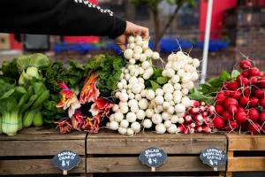 A customer picks up a bundle of salad turnips at the Radicle Roots Farm booth at the Snohomish Farmers Market on Thursday, May 5, 2022 in Snohomish, Washington. (Olivia Vanni / The Herald)