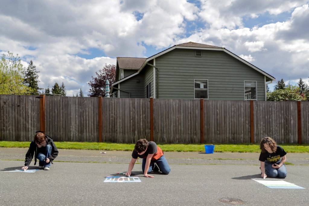 Mia Shields, Sam Bowles and Rhyanna Mercer produce chalk drawings to be washed away by a bucket of water for TikTok videos. (Kevin Clark / The Herald)