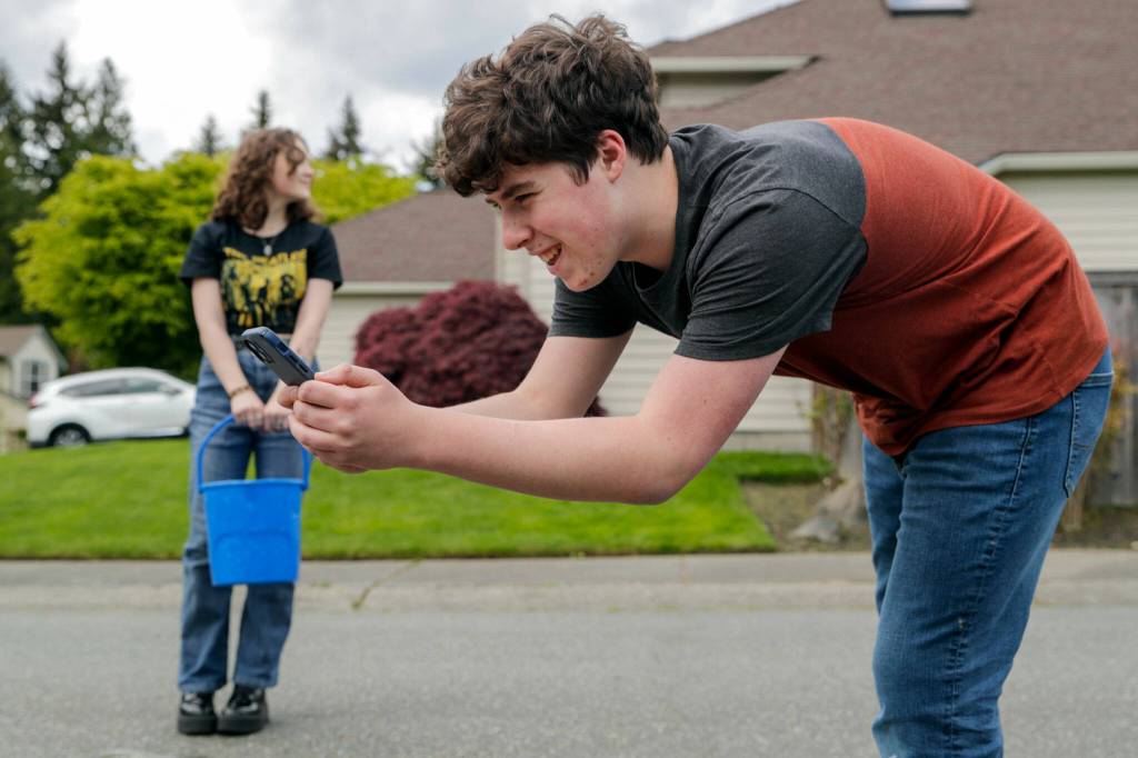 Sam Bowles records the runoff of the water from a chalk drawing with friend and co-artist, Rhyanna Mercer. (Kevin Clark / The Herald)