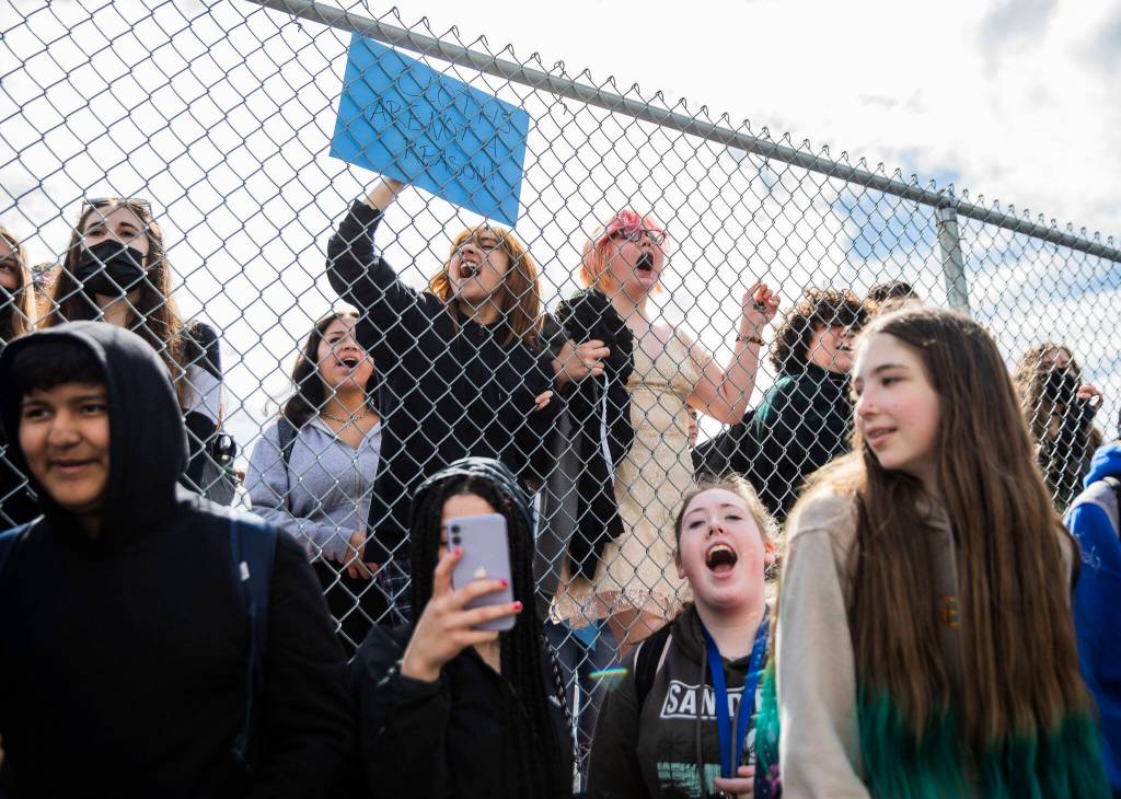 North Middle School eighth graders Cynthia Espinoza (left) and Fern Conroy (right) chant with Everett High School students from the other side of a perimeter fence surrounding the middle school on Monday. (Olivia Vanni / The Herald)