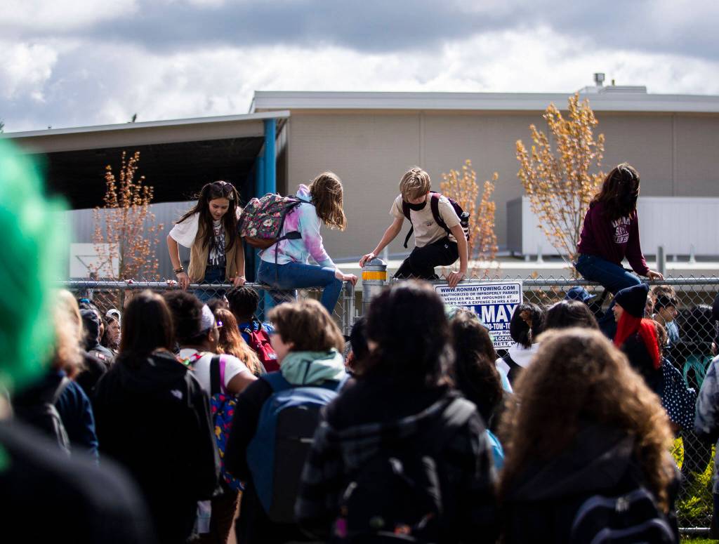 North Middle School students hop over a perimeter fence to join Everett High School students in their walkout on Monday. (Olivia Vanni / The Herald)