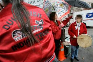 Barbara Williams, center, holds an umbrella for her mother, tribal chair Cecile Hansen, right, as they prepare to join other members of the Duwamish Indian Tribe in performing an "honor song" Wednesday, Feb. 27, 2008 near a location in Seattle where bones were found during construction activities near the Pike Place Market. The song was performed because the tribe felt at the time that the remains could have been from an ancient member of the tribe, but city authorities said later in the day that the remains appeared to have been from a small animal. (AP Photo/Ted S. Warren)