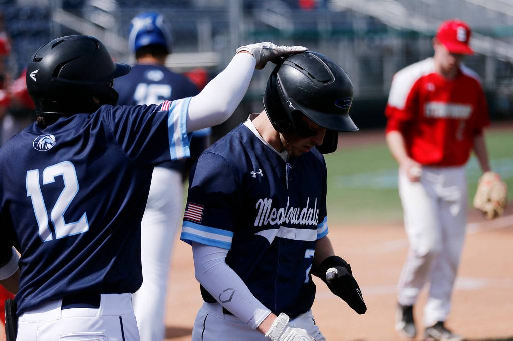 Meadowdales Nicholas Banez pats the helmet of teammate Nicholas Blas after Blas scored a 7th-inning run against Stanwood Saturday, May 14, 2022, during a 3A district matchup at Funko Field in Everett, Washington. (Ryan Berry / The Herald)