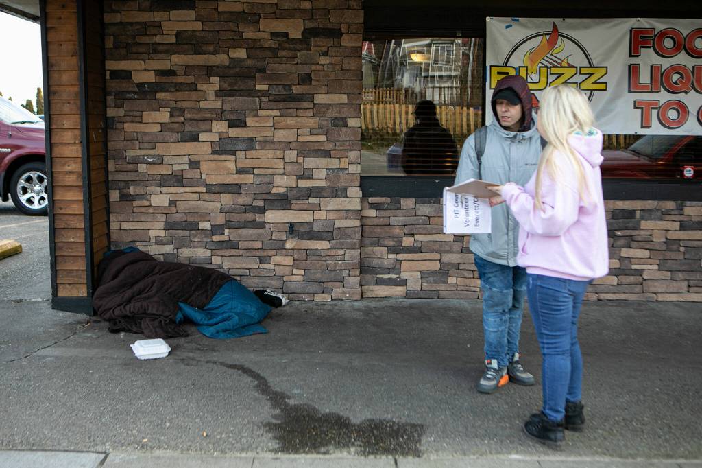 A person sleeps on the ground as Mandy Jeffcott speaks with a man experiencing homelessness Feb. 22 in Everett. (Ryan Berry / The Herald)