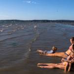 Melissa Simons, right, holds Jet Juliann, 3, while Ashley Allege, center, watches Lincoln Ballard, 3, swim in the water off of Jetty Island on Thursday, July 5, 2018 in Everett, Wa. (Olivia Vanni / The Herald)