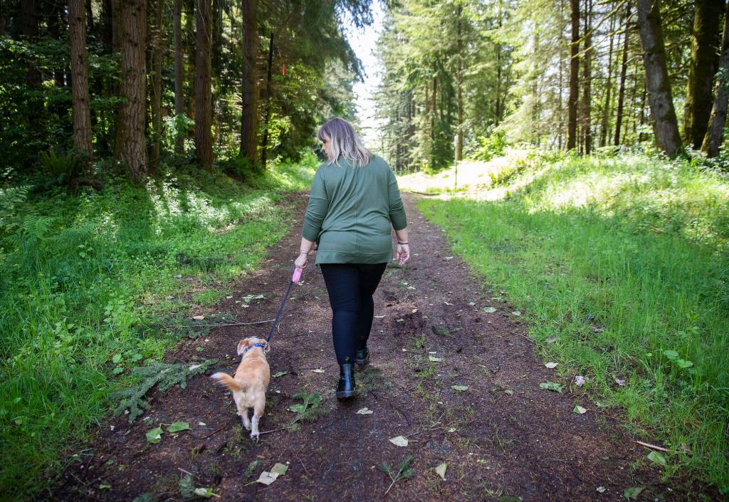 April Provost and her dog Odie walk through land behind Walmart in Monroe known for encampments on May 25. (Olivia Vanni / The Herald)