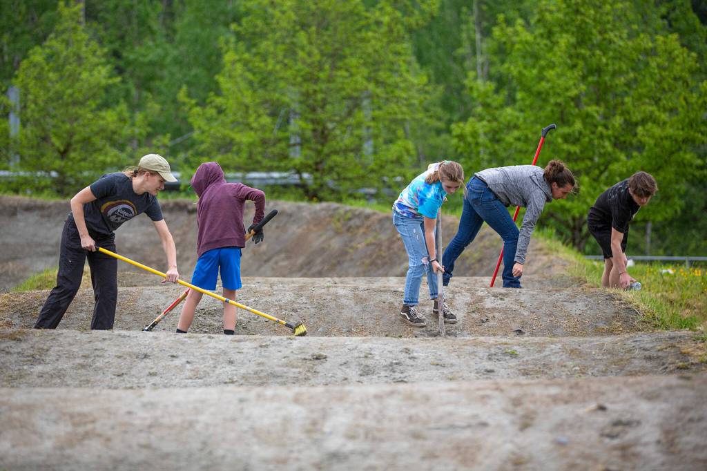 Members of Bigfoot BMX and their children rake and sweep a portion of the track as they prepare for the season on Wednesday. (Ryan Berry / The Herald)