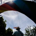 A person wearing a small rainbow flag on their hat passes under a rainbow arch at Arlingtons first-ever Pride celebration Saturday. (Olivia Vanni / The Herald)