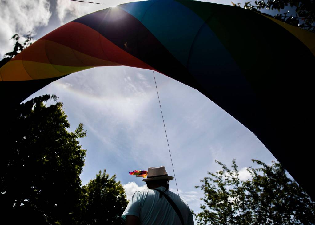 A person wearing a small rainbow flag on their hat passes under a rainbow arch at Arlingtons first-ever Pride celebration Saturday. (Olivia Vanni / The Herald)