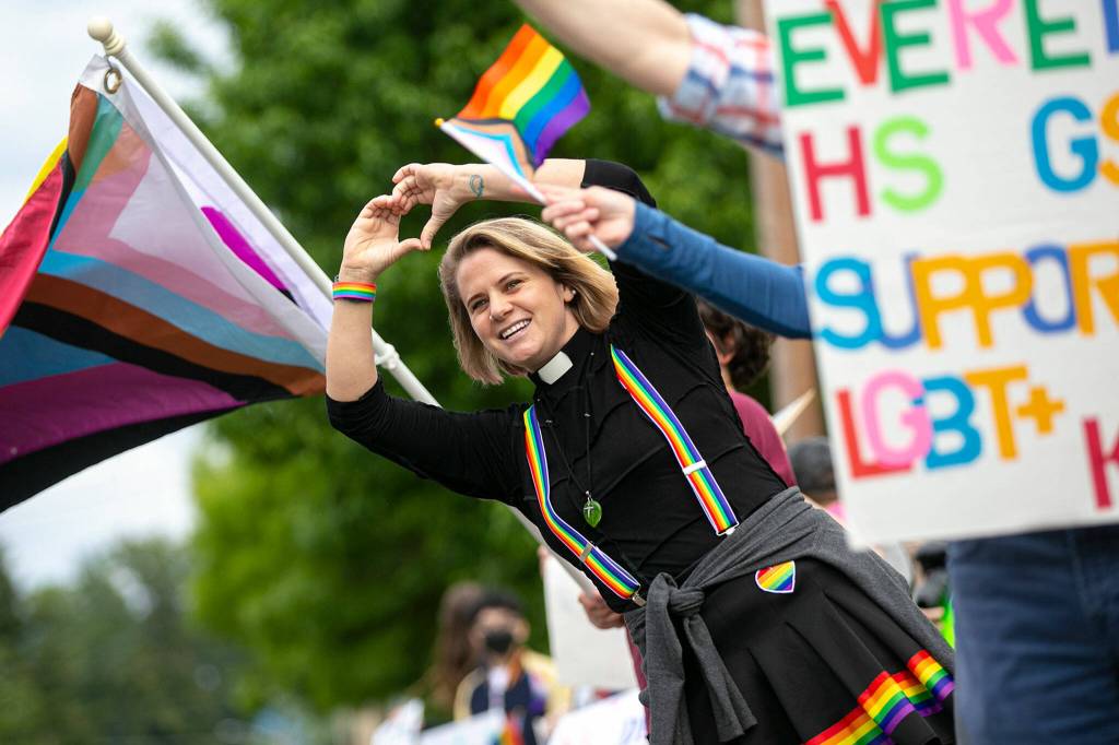 Reverend Kate Kilroy makes a heart with her hands towards passing vehicles during a rally backing LGBTQ+ students on Monday in front of the Marysville School District Service Center in Marysville. (Ryan Berry / The Herald)