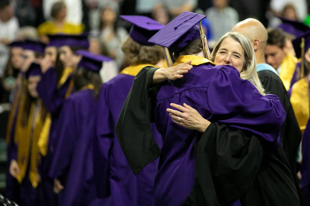 Staff members hug students as they take their seats during Lake Stevens High Schools 2022 commencement ceremony Tuesday at Angel of the Winds Arena in Everett. (Ryan Berry / The Herald)