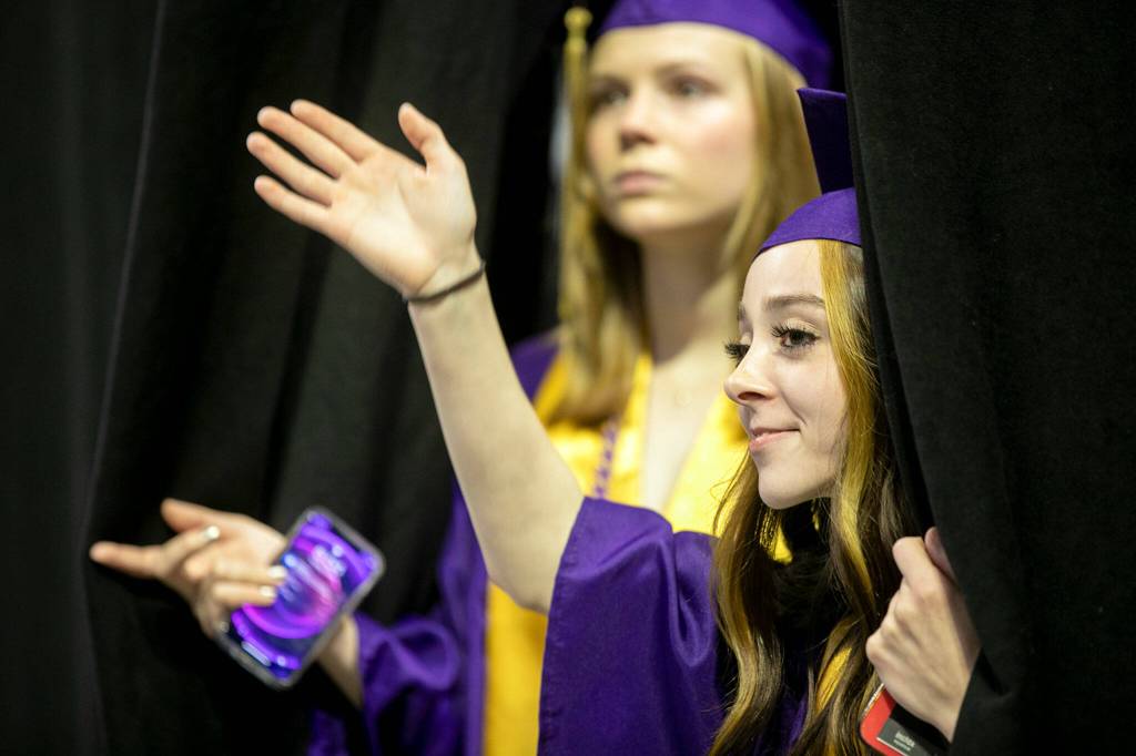 Students peek through the stage curtain to find family before Lake Stevens High Schools 2022 commencement ceremony Tuesday at Angel of the Winds Arena in Everett. (Ryan Berry / The Herald)