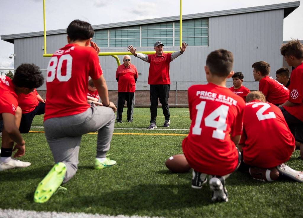 Mike Price (left) listens while his sonl, Eric, walks through a drill with the players the attending Price Elite Passing Academy on Wednesday at Bagshaw Field in Everett. (Olivia Vanni / The Herald)