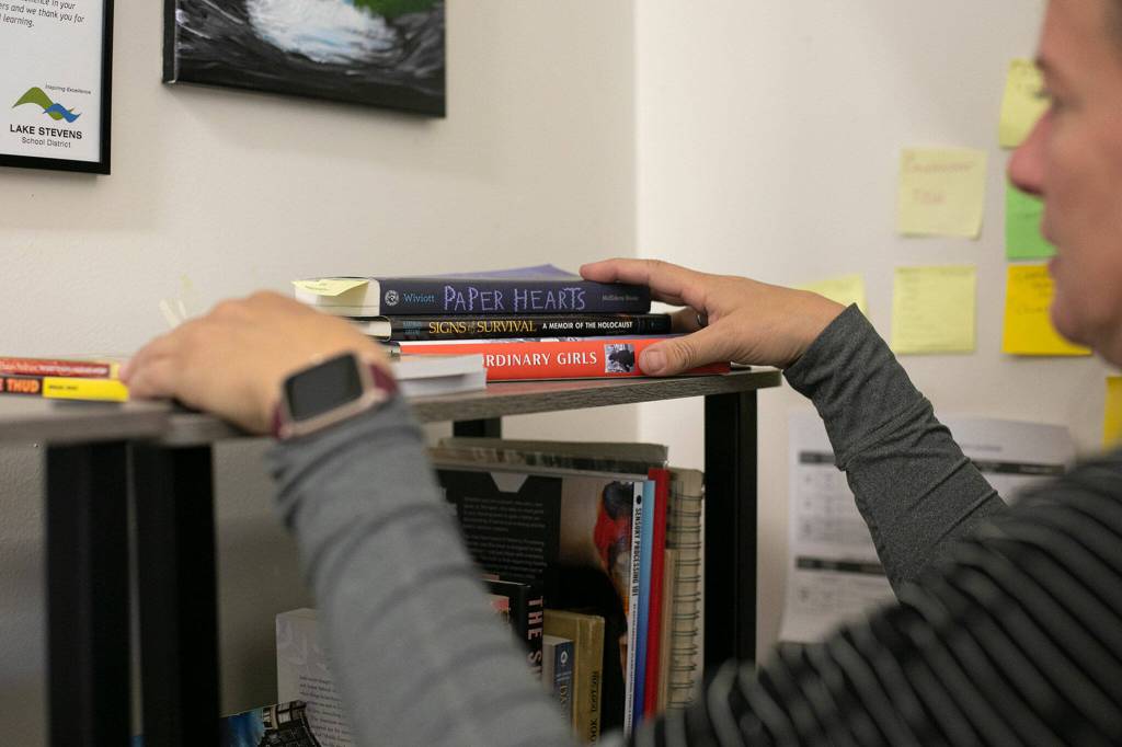 Emily Dykstra, an 8th grade English teacher at Cavelero Mid High School, rifles through the different books at her desk, many of which cover the Holocaust, on Wednesday in Lake Stevens. (Ryan Berry / The Herald)