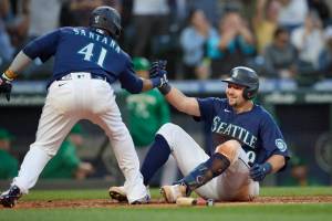 Seattle Mariners' Carlos Santana helps Cal Raleigh at home after they scored against the Oakland Athletics during the fifth inning of a baseball game, Thursday, June 30, 2022, in Seattle. Raleigh hit a two-run triple and scored on a throwing error. (AP Photo/John Froschauer)