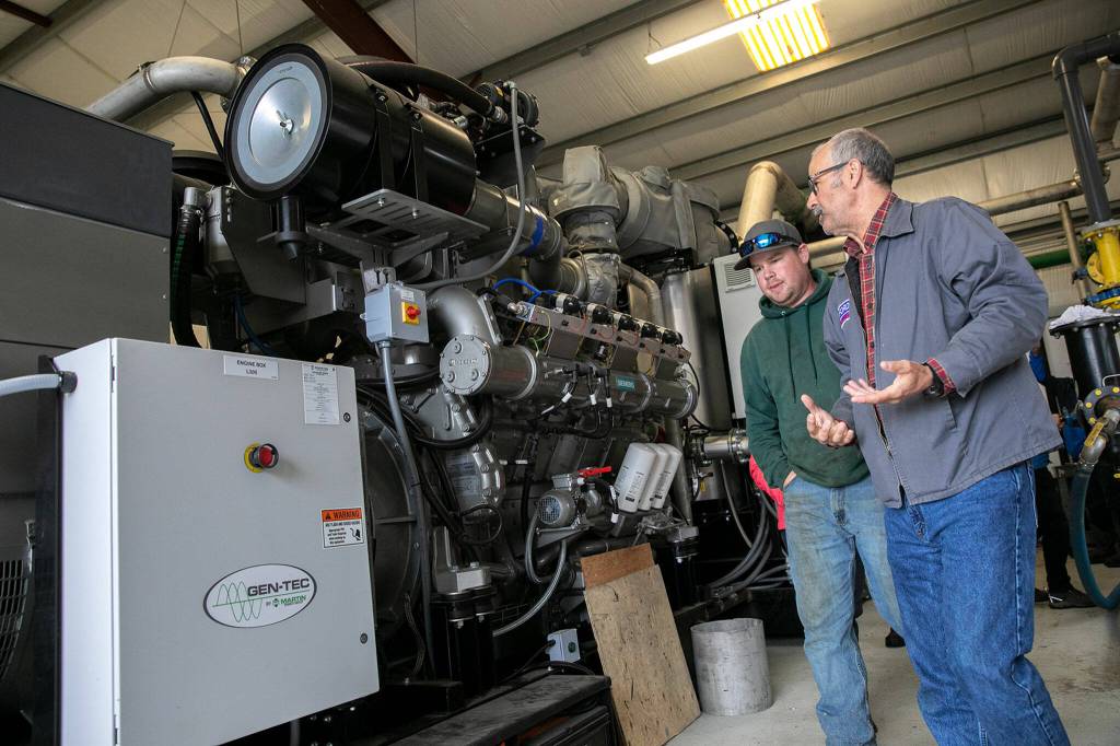 Jon Van Nieuwenhuyzen walks with a person past the new generator as it is being installed on June 17 in Monroe. (Ryan Berry / The Herald)
